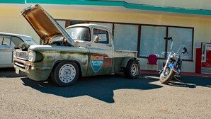 A vintage truck with its hood open parked in front of a building with a sign that reads "Raton Pass".