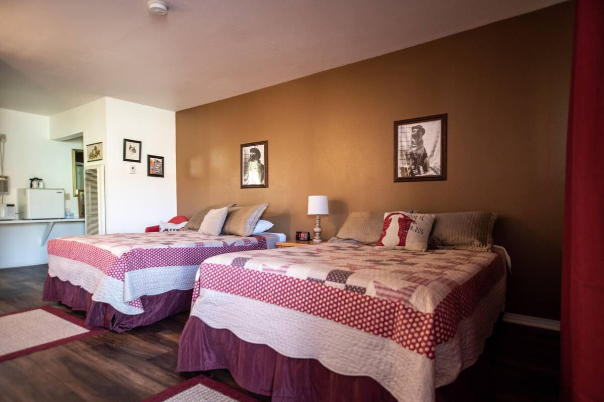 A hotel room with two beds, a small desk, and a kitchenette.