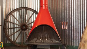 A red wood stove with a chimney, a large wooden wheel, and a fur rug on the floor.
