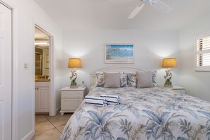 A bedroom with a bed, two nightstands, a ceiling fan, a painting, and a bathroom visible through an open door. - Casa Del Mar Longboat Key (Longboat Key)