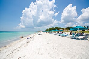 A beach with white sand, clear turquoise water, and a row of blue umbrellas. - Casa Del Mar Longboat Key (Longboat Key)