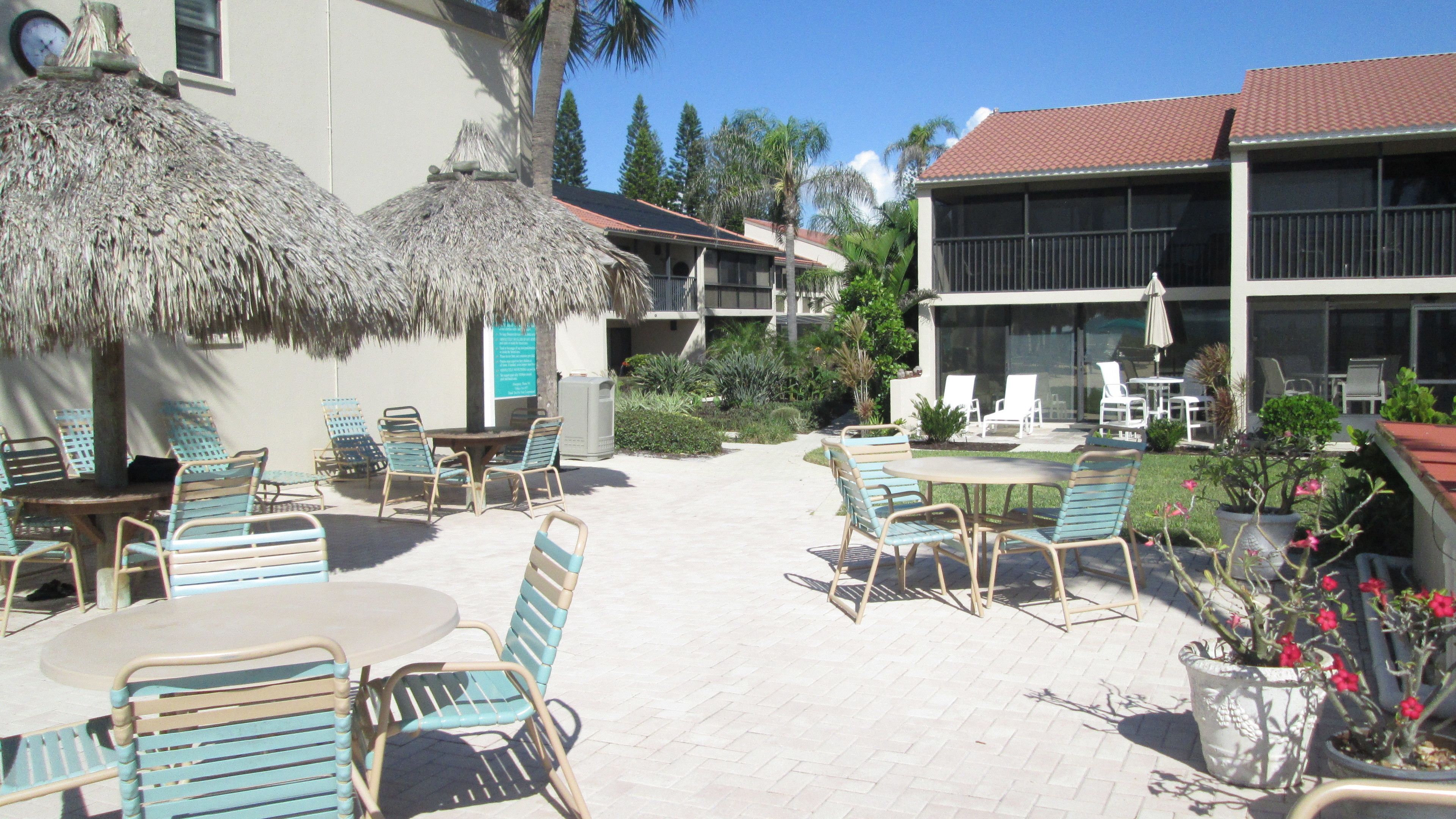 A courtyard with outdoor seating, a thatched umbrella, and a building with a red-tiled roof.