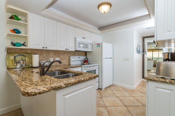 A kitchen with white cabinets, a granite countertop, a microwave, a stove, and a refrigerator.