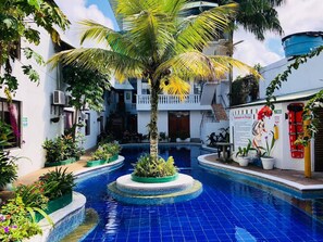 Uma área de piscina com uma palmeira, rodeada por plantas em vasos e um mural.