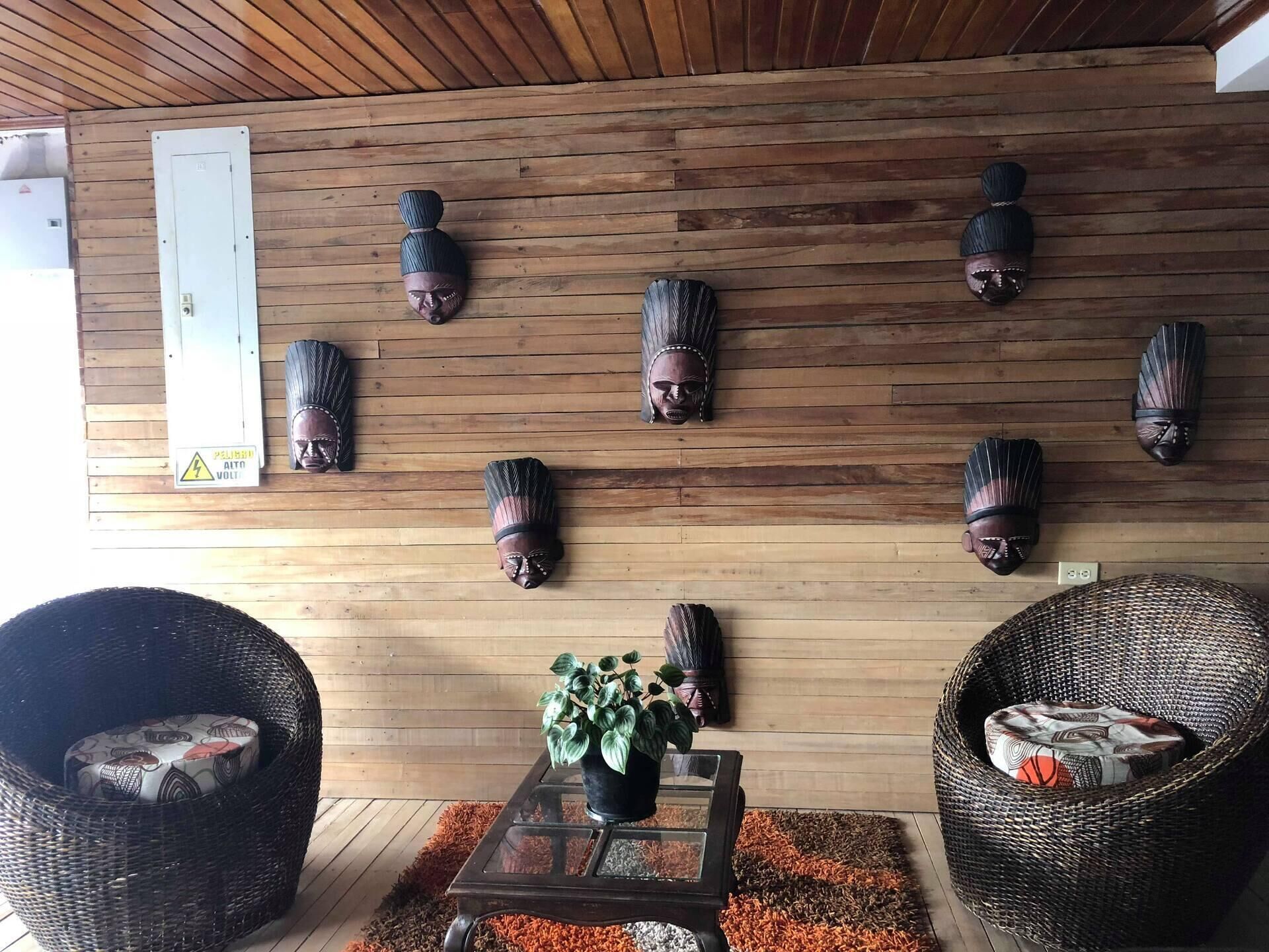 Une pièce aux murs en bois, une table avec un plateau en verre sur laquelle est posée une plante en pot, et deux fauteuils en osier ornés de coussins à motifs.