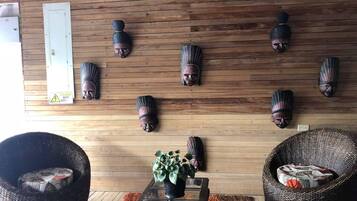 Une pièce aux murs en bois, une table avec un plateau en verre sur laquelle est posée une plante en pot, et deux fauteuils en osier ornés de coussins à motifs.