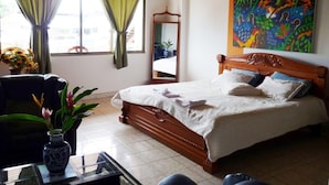 A hotel room with a wooden bed, a mirror, a colorful abstract painting, and a vase with flowers. - Hotel Yurupary (Leticia)