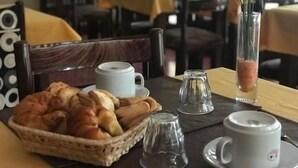 A dining table with a basket of croissants, two white cups, and a glass pitcher. - Hotel Resi San Bernardo (San Bernardo del Tuyú)