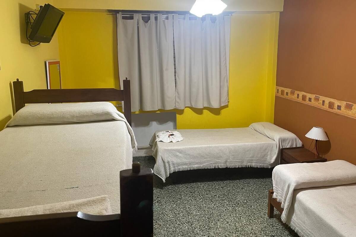 Habitación de hotel con dos camas, ventilador de techo, televisor montado en la pared y ventana con cortinas.