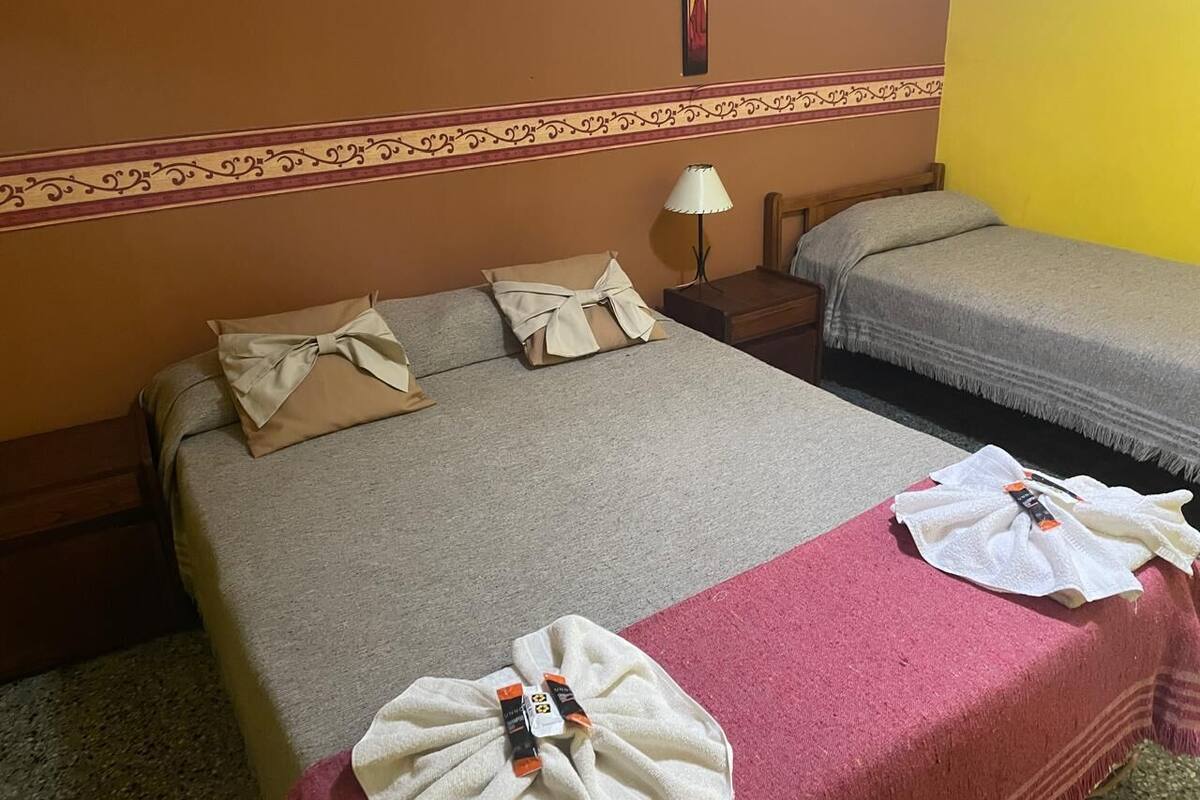 Habitación de hotel con dos camas, una mesita de noche, una lámpara y un borde decorativo en la pared.