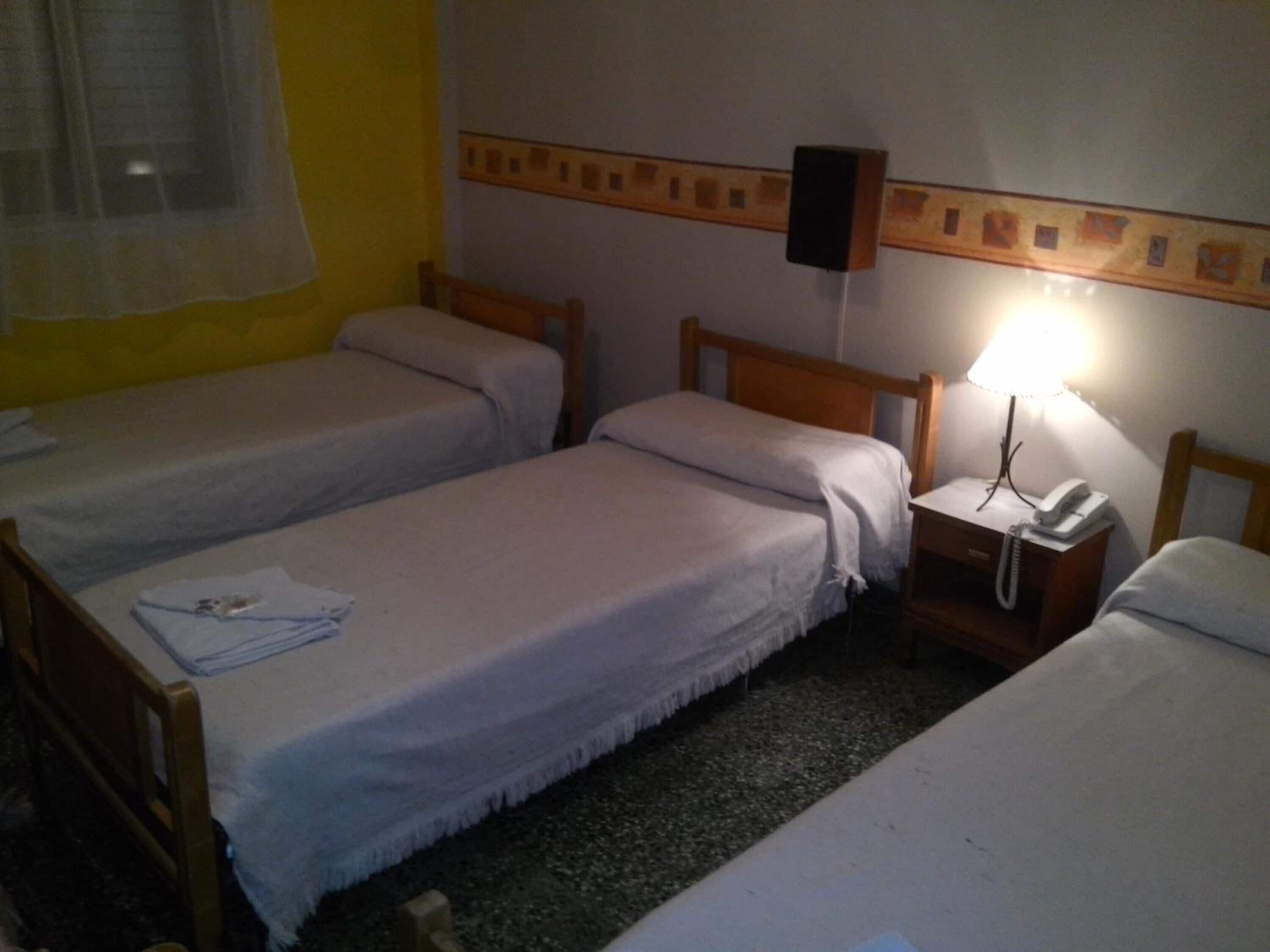 A hotel room with two single beds, a bedside table with a lamp, a telephone, and a wall-mounted speaker.