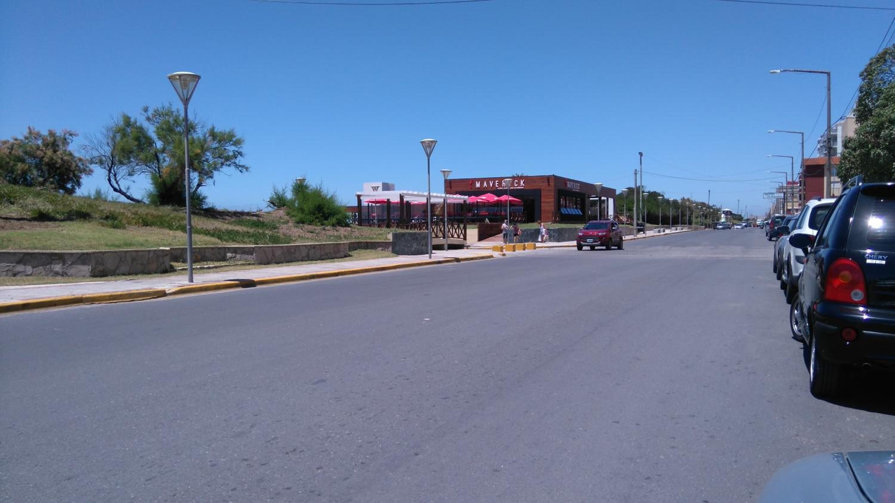 A street view with a building labeled "MAVERICK" in the distance, featuring outdoor seating with umbrellas.