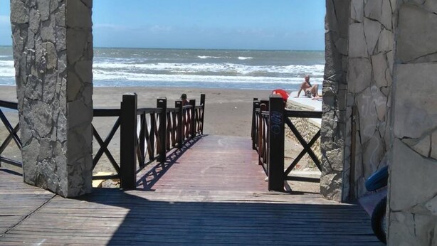 A wooden boardwalk leading to a beach with stone pillars and a wooden roof structure. - Hotel Resi San Bernardo (San Bernardo del Tuyú)