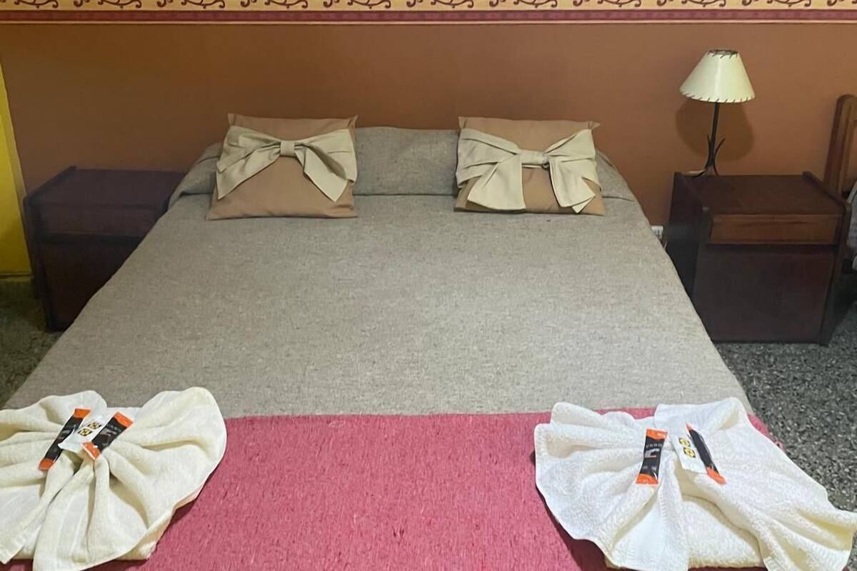 Una cama bien hecha con una colcha roja y dos toallas dobladas sobre ella.