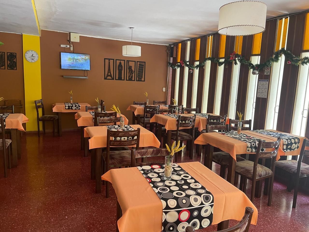 A restaurant with multiple tables covered in orange tablecloths, wooden chairs, and a decorative centerpiece.