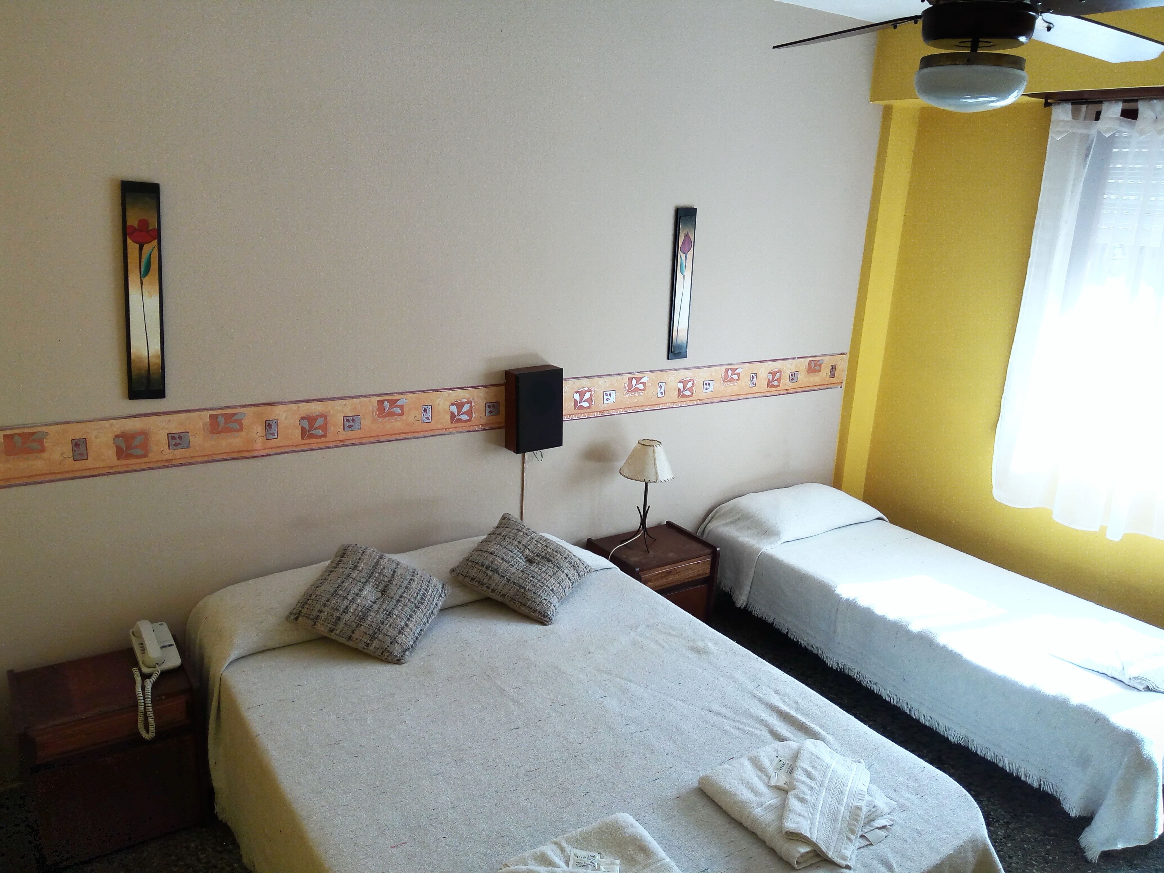 A hotel room with two beds, a ceiling fan, a bedside lamp, a telephone, and a decorative wall border.
