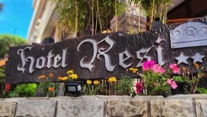 A hotel sign with the name 'Hotel Residencia' and a stone wall with flowers in front. - Hotel Resi San Bernardo (San Bernardo del Tuyú)