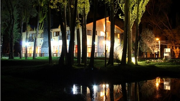Ein zweistöckiges Gebäude mit einem Teich davor, umgeben von Bäumen und beleuchtet von Straßenlaternen.