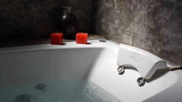 Una bañera con dos velas rojas y un florero negro.