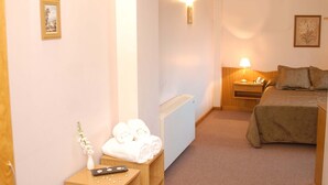 Habitación de hotel con cama, mesita de noche, lámpara y un taburete de madera con toallas.