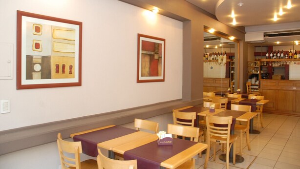 Un restaurante con mesas y sillas de madera, obras de arte en las paredes y una zona de bar con botellas y vasos.