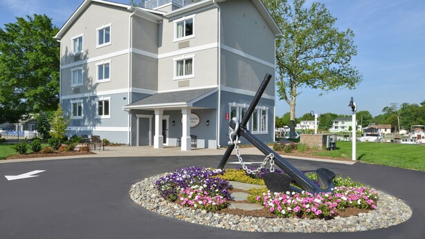 Un hotel de varios pisos con una entrada central, un jardín ajardinado con flores y una escultura de metal.