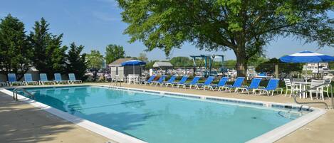 A rectangular swimming pool with a tiled edge, surrounded by blue lounge chairs and white tables.