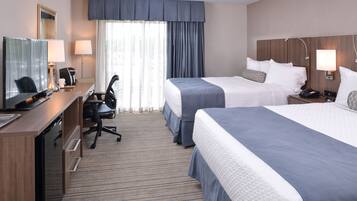 A hotel room with two beds, a desk with a computer, a chair, and a TV.