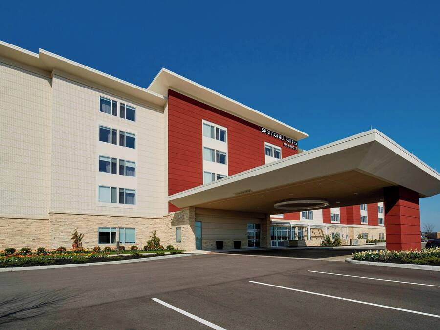 A modern hotel with a red and beige facade, a covered entrance, and a parking lot.
