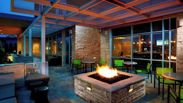 An outdoor patio area with a stone fire feature, green seating, and large windows overlooking the street.