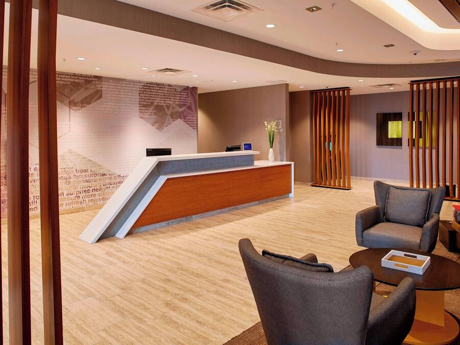 A modern reception area with a wooden reception desk, grey upholstered chairs, and a small table with a tray.