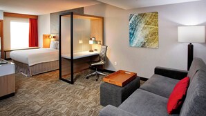 A hotel room with a bed, desk, chair, sofa, and artwork on the wall.