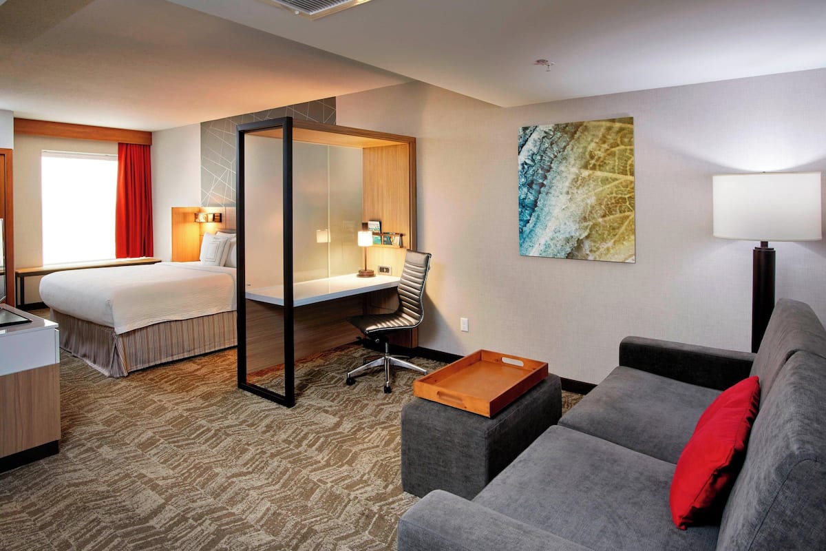 Une chambre d’hôtel comprenant un lit, un bureau, une chaise, un canapé et une œuvre d’art au mur.