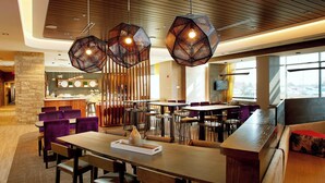 A modern restaurant with wooden tables and purple chairs, a bar area, and large windows with a view.