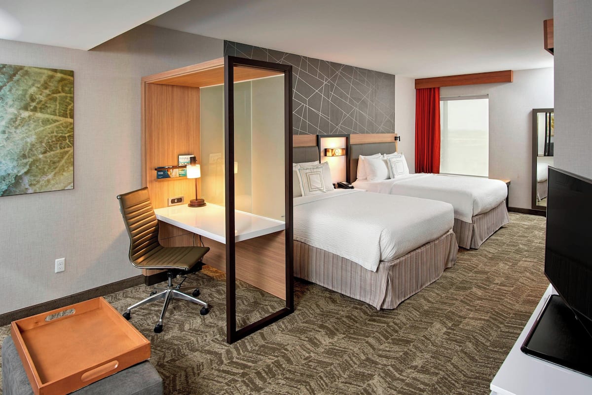 Une chambre d’hôtel équipée d’un bureau, de deux lits, d’une télévision et d’une petite commode en bois.