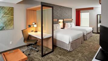A hotel room with a desk, two beds, a TV, and a small wooden chest.
