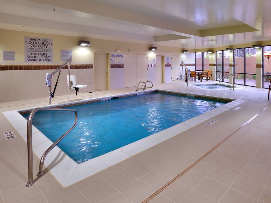 An indoor swimming pool with safety signs, a lifeguard chair, and a seating area with tables and chairs.