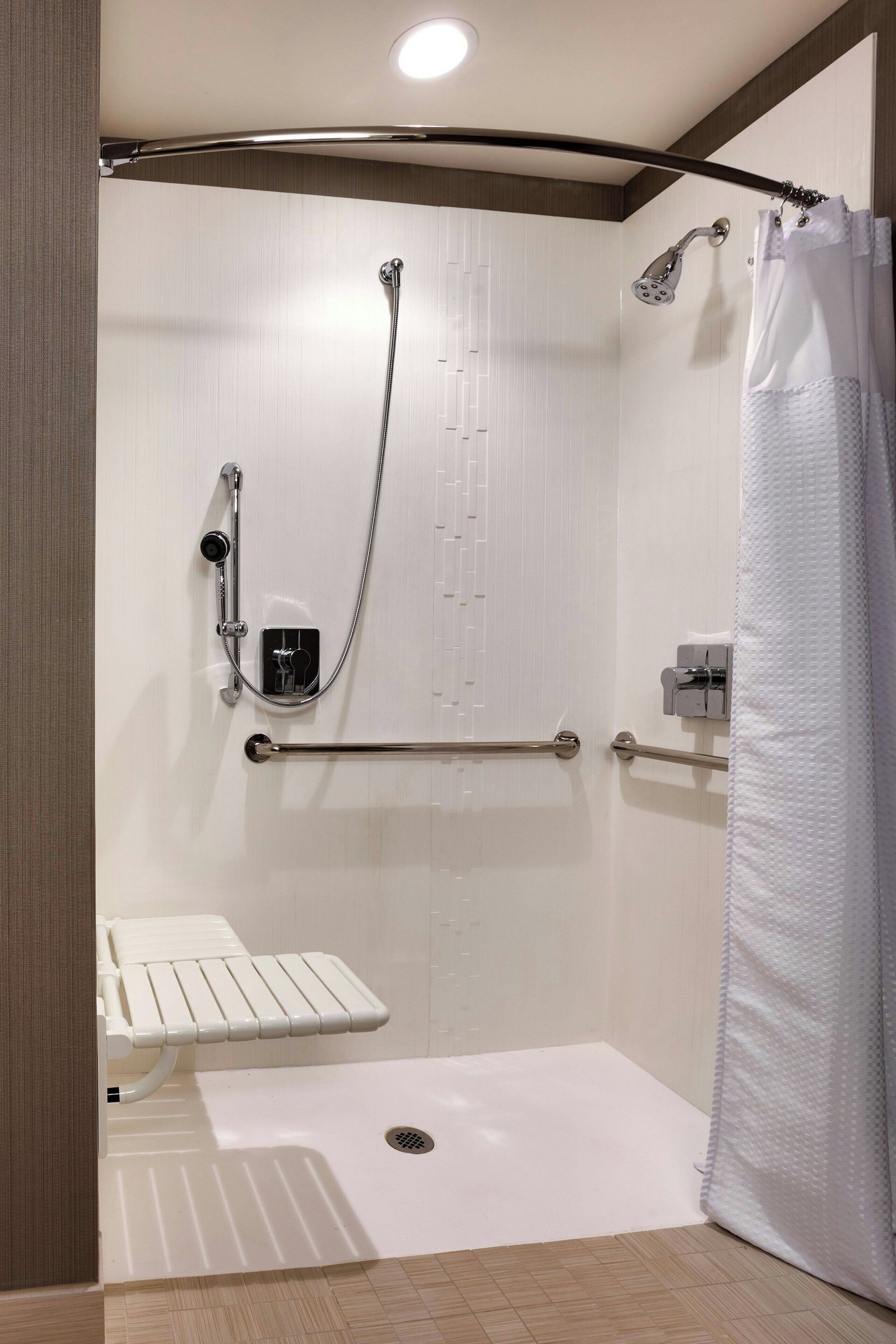 A modern shower area with a grab bar, a handheld showerhead, and a white shower curtain.