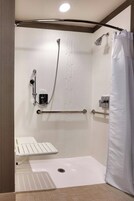 Un área de ducha moderna con una barra de apoyo, un cabezal de ducha de mano y una cortina de ducha blanca.