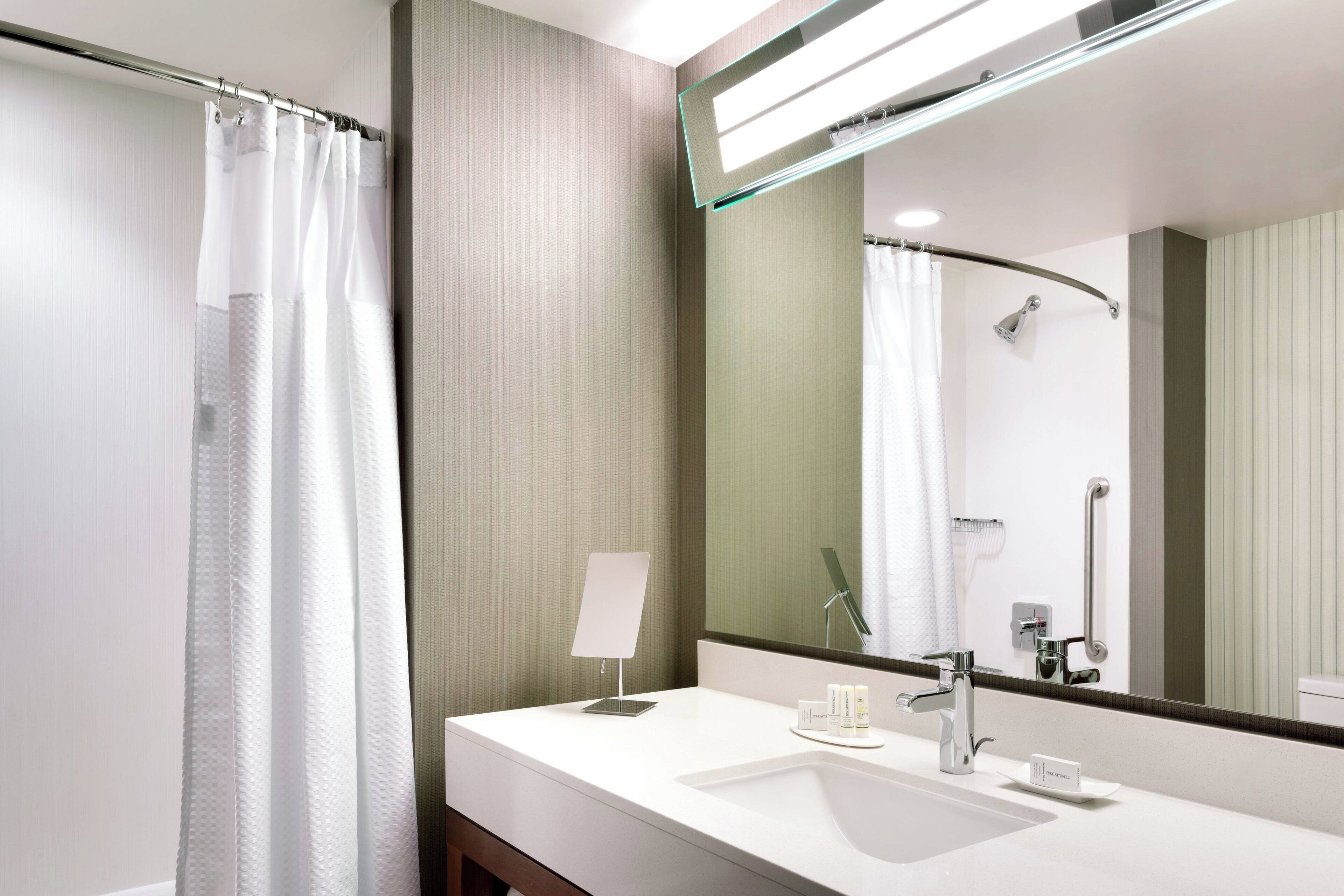 A modern bathroom with a white sink, a mirror, a shower curtain, and a handheld showerhead.