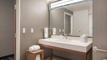 A modern bathroom with a large mirror, two sinks, and a wooden shelf with towels.