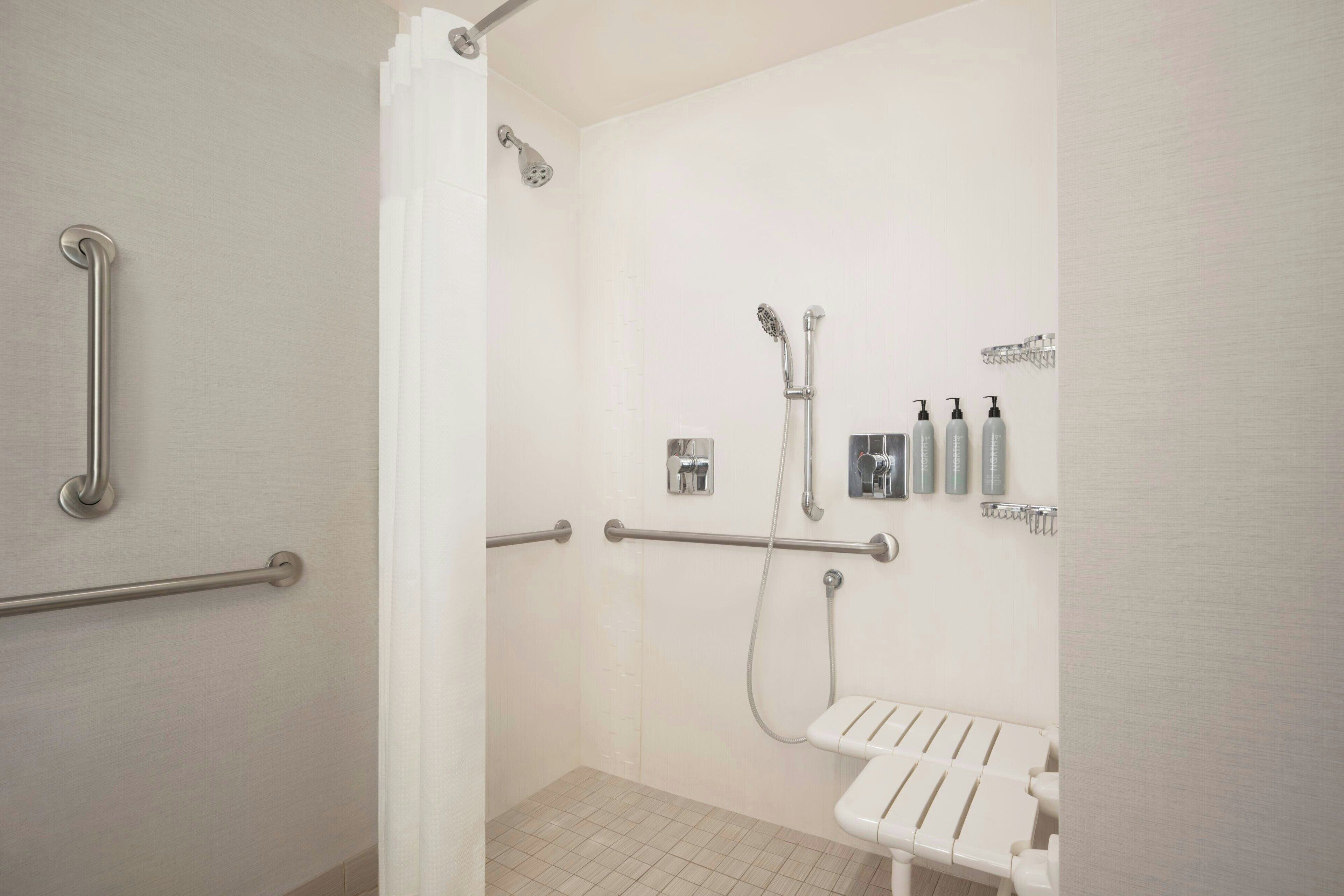 A bathroom with a shower, grab bars, a white sink, and toiletries on the wall.