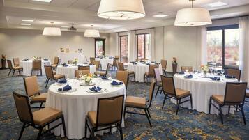 A conference room with multiple round tables, each set with chairs, white tablecloths, and blue napkins.