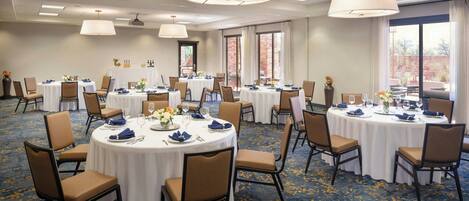 A conference room with multiple round tables, each set with chairs, white tablecloths, and blue napkins.
