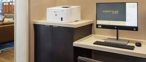 A hotel reception desk with a computer monitor displaying the Courtyard by Marriott logo, a printer, a keyboard, and a chair.