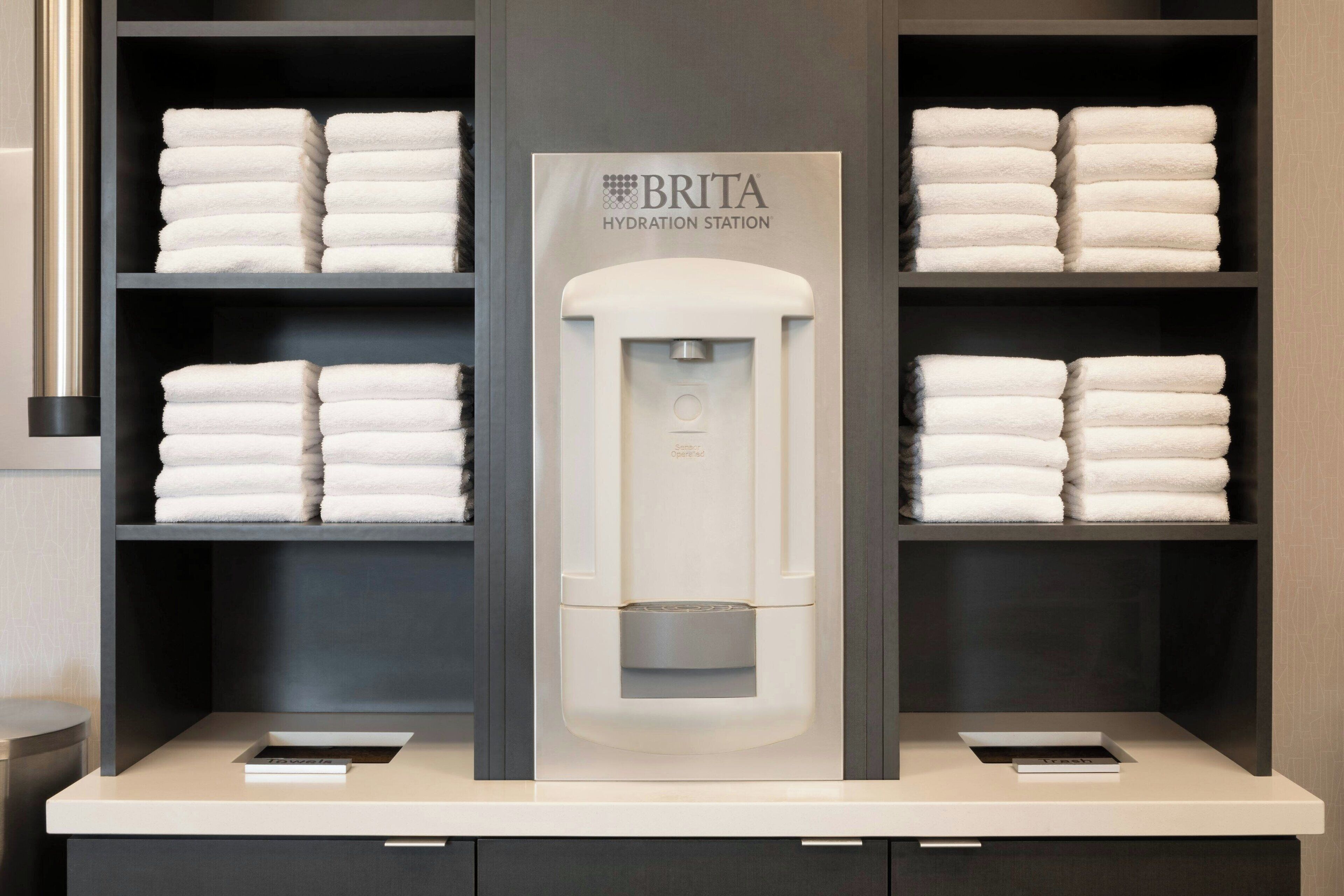 A BRITA hydration station in a hotel bathroom with neatly stacked towels on shelves.