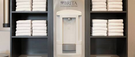 A BRITA hydration station in a hotel bathroom with neatly stacked towels on shelves.
