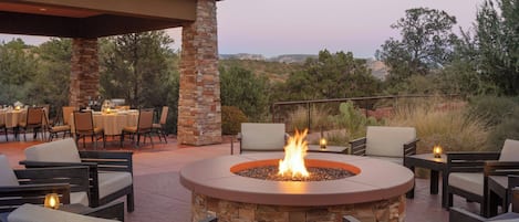 An outdoor patio with a stone fire pit, seating, and tables.