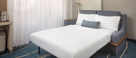 A hotel room with a bed, a nightstand, a lamp, and a window with curtains.