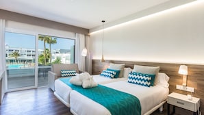 Une chambre d’hôtel moderne avec un grand lit, une table de chevet avec une lampe, et une vue sur une piscine et des immeubles.